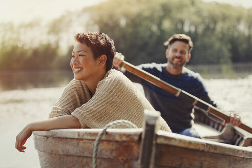 Smiling couple canoeing on sunny lake - CAIF10703