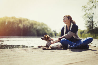 Smiling woman and dog relaxing on sunny lakeside dock - CAIF10708