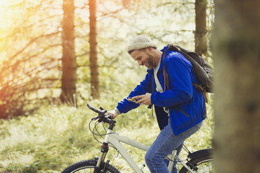 Mann fährt Mountainbike und schreibt mit Handy im Wald - CAIF10709