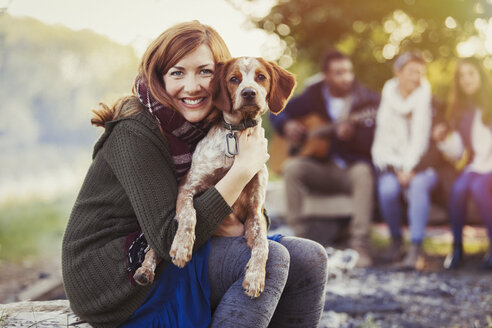 Portrait smiling woman hugging dog at campsite with friends - CAIF10712