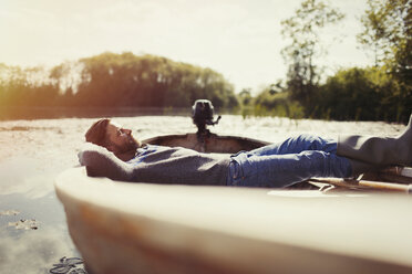 Serene man laying relaxing in canoe on sunny lake - CAIF10714
