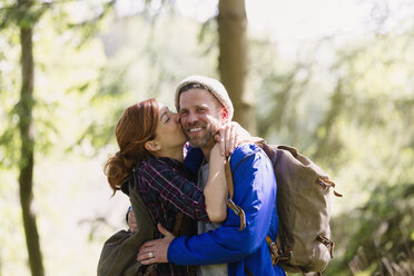 Portrait smiling couple kissing hiking in woods - CAIF10718