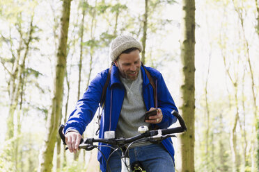 Mann fährt Mountainbike und schreibt mit Handy im Wald - CAIF10721