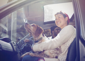 Smiling woman holding dog on lap in car - CAIF10730