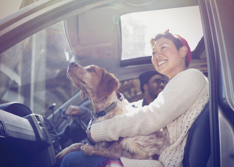 Lächelnde Frau mit Hund auf dem Schoß im Auto - CAIF10730