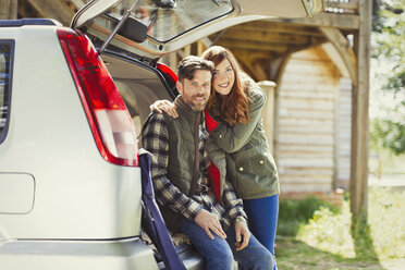 Portrait smiling couple at back of car outside cabin - CAIF10731