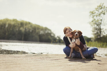 Porträt lächelnde Frau umarmt Hund auf sonnigen Steg am See - CAIF10747