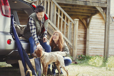 Ehepaar mit Hund auf dem Rücksitz eines Autos vor einer Hütte - CAIF10752
