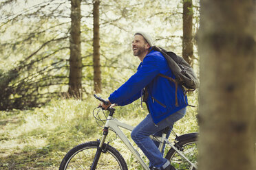 Lächelnder Mann beim Mountainbiking im Wald - CAIF10755