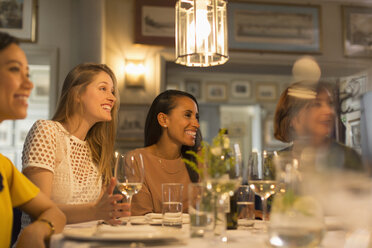 Lächelnde Freundinnen, die beim Essen und Trinken von Weißwein am Restauranttisch wegschauen - CAIF10774