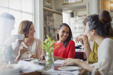Smiling women friends dining drinking coffee at restaurant table - CAIF10789