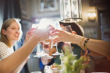 Lächelnde Freundinnen stoßen mit Weingläsern an einem Restauranttisch an - CAIF10795
