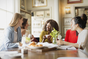 Smiling women drinking coffee and talking at restaurant table - CAIF10796