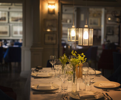 Illuminated pendant lights over placesettings on restaurant table - CAIF10799