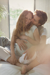 Zärtliches schwangeres Paar, das sich auf dem Bett küsst - CAIF10808
