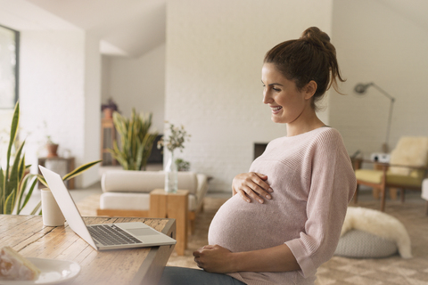 Schwangere Frau bei einer Videokonferenz am Laptop, lizenzfreies Stockfoto