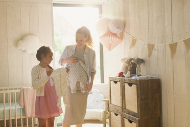 Pregnant mother and daughter holding baby clothes in nursery - CAIF10811