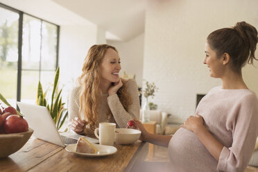 Schwangere Frauen essen Kuchen und Obst am Laptop im Esszimmer - CAIF10813