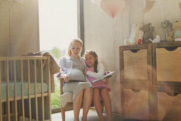 Schwangere Mutter und Tochter lesen ein Märchenbuch im Kinderzimmer - CAIF10832