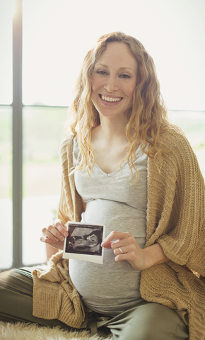 Porträt einer lächelnden schwangeren Frau, die ein Ultraschallbild hält, lizenzfreies Stockfoto