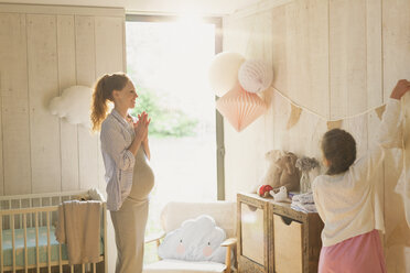 Schwangere Mutter und Tochter dekorieren ein sonniges Kinderzimmer - CAIF10857