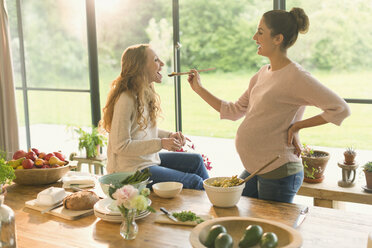 Schwangere Frauen beim Kochen und Probieren von Speisen am Tisch - CAIF10861