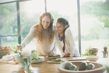 Smiling mother and daughter preparing food - CAIF10873