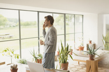 Man in pajamas talking on cell phone and drinking coffee - CAIF10904