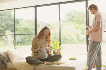 Ein schwangeres Paar isst und trinkt Kaffee im Wohnzimmer - CAIF10906