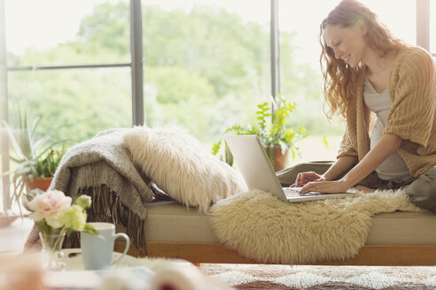 Schwangere Frau mit Laptop auf der Chaiselongue im Wohnzimmer - CAIF10907