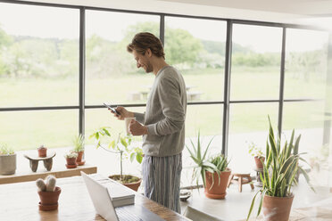 Man in pajamas drinking coffee and texting with cell phone - CAIF10909