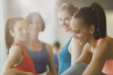 Lächelnde Frauen unterhalten sich in einem sonnigen Fitnessstudio - CAIF10927