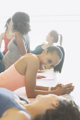 Lächelnde Frauen, die sich auf Yogamatten in einem Fitnessstudio unterhalten - CAIF10936