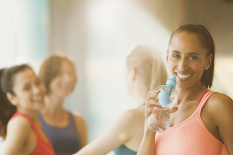 Porträt lächelnde Frau trinkt Wasser im Fitnessstudio, lizenzfreies Stockfoto