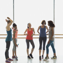 Lächelnde Frauen unterhalten sich und trinken Wasser an der Stange im Fitnessstudio - CAIF10947