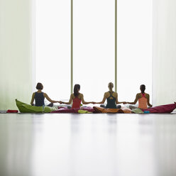 Frauen auf Kissen halten sich am Fenster in einem Studio für Entspannungsyoga an den Händen - CAIF10973