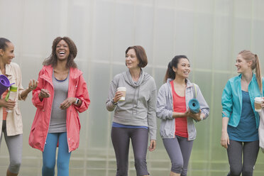 Lächelnde Frauen, die mit Yogamatten und Kaffee spazieren gehen - CAIF10975