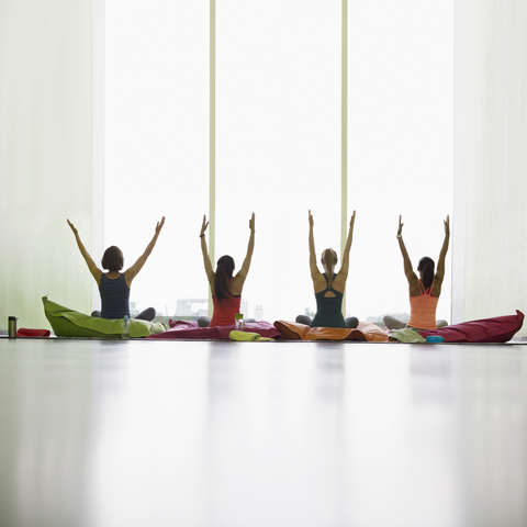 Women on cushions with arms raised in restorative yoga gym studio stock photo