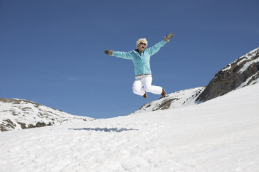 Exuberant woman jumping in snow - CAIF11007