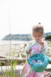 Mädchen sammelt Ostereier in einem Korb am Strand - CAIF11060