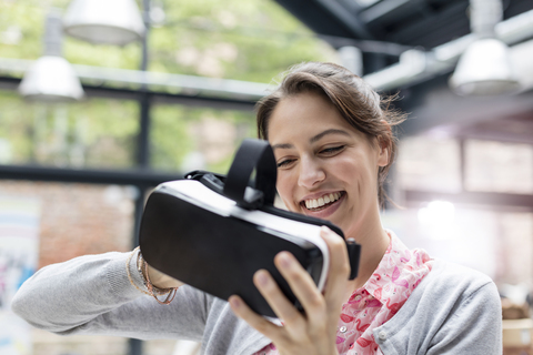 Lächelnde Frau, die auf einer Technologiekonferenz eine Virtual-Reality-Simulatorbrille ausprobiert, lizenzfreies Stockfoto