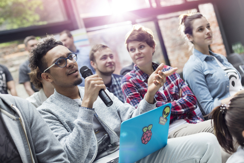 Mann im Publikum mit Laptop stellt auf einer Konferenz eine Frage mit Mikrofon, lizenzfreies Stockfoto