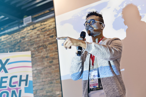 Redner mit Mikrofon vor einer Projektionsfläche bei einer Technologiekonferenz, lizenzfreies Stockfoto