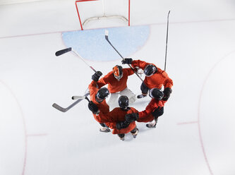Draufsicht auf eine Eishockeymannschaft in roten Trikots, die sich auf dem Eis zusammentut - CAIF11149