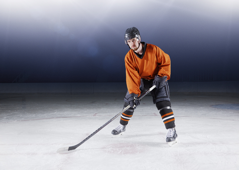 Porträt selbstbewusster Eishockeyspieler in orangefarbener Uniform auf dem Eis, lizenzfreies Stockfoto