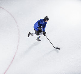 Eishockeyspieler in blauer Uniform beim Schlittschuhlaufen mit Puck auf dem Eis - CAIF11168