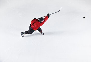 Eishockeyspieler in roter Uniform schießt Puck auf Eis - CAIF11175