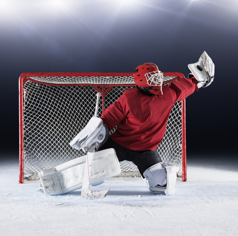 Hockeytorwart in roter Uniform, der mit seinem Handschuh nach dem Puck im Tornetz greift, lizenzfreies Stockfoto