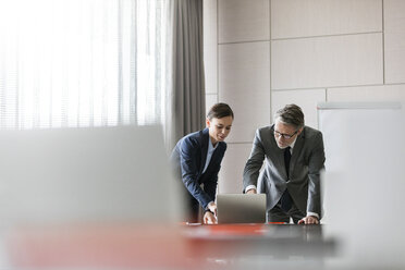 Businessman and businesswoman using laptop in conference room - CAIF11183