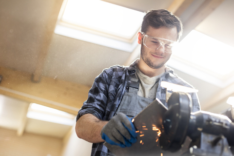 Lächelnder Metallarbeiter beim Schleifen in der Werkstatt, lizenzfreies Stockfoto